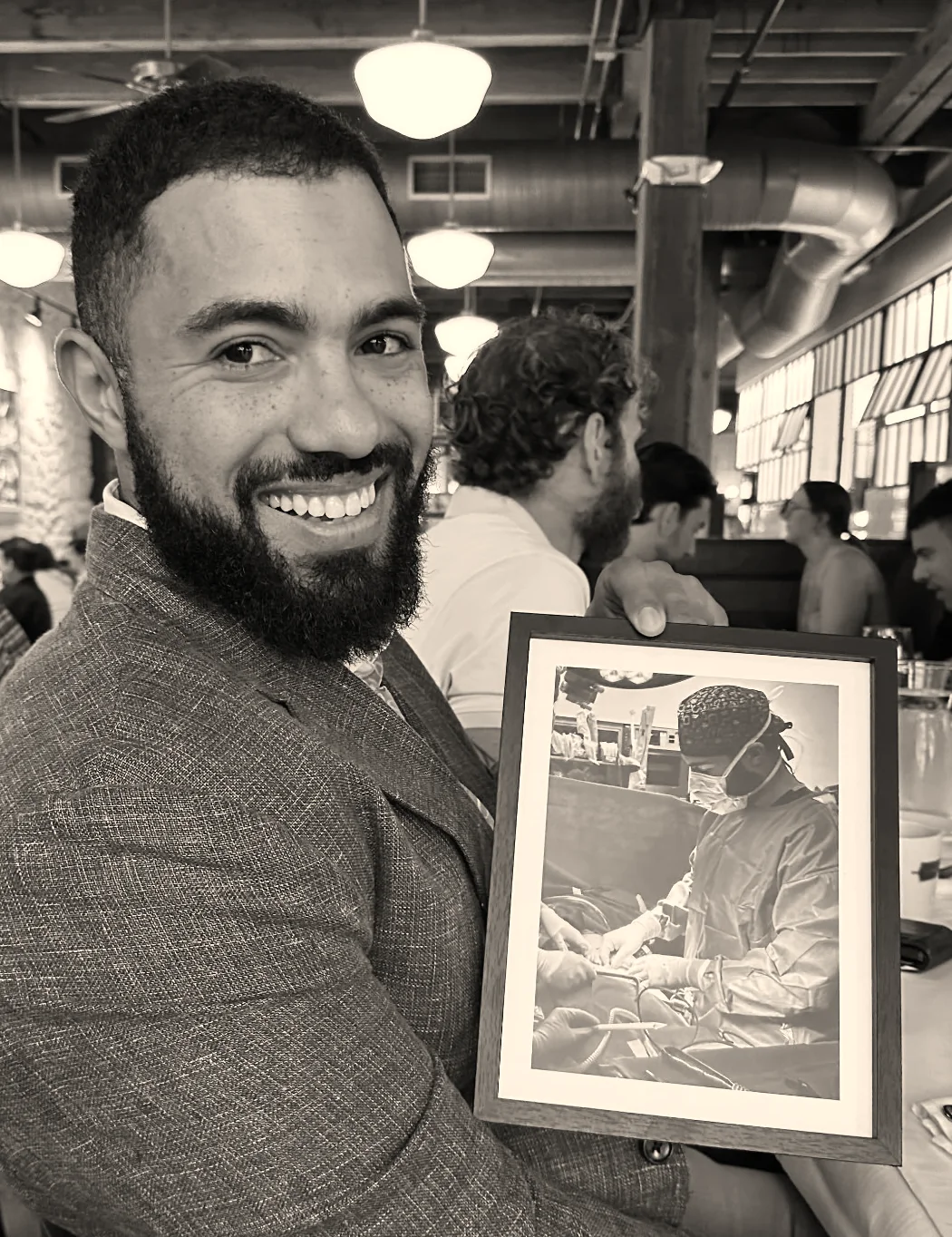Dr. Jeremy Goodman smiling, holding a framed photo of himself operating